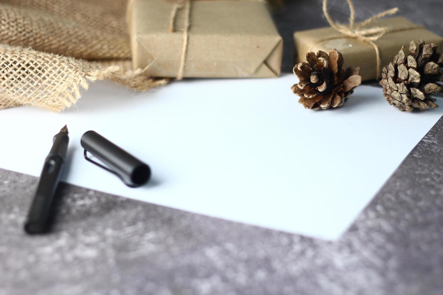 Feiertagsgeschenke. weihnachten und neujahr. geschenkbox in braunes papier tannenzapfen und weißes papier und stifte auf den tisch gelegt, kopierraum. foto