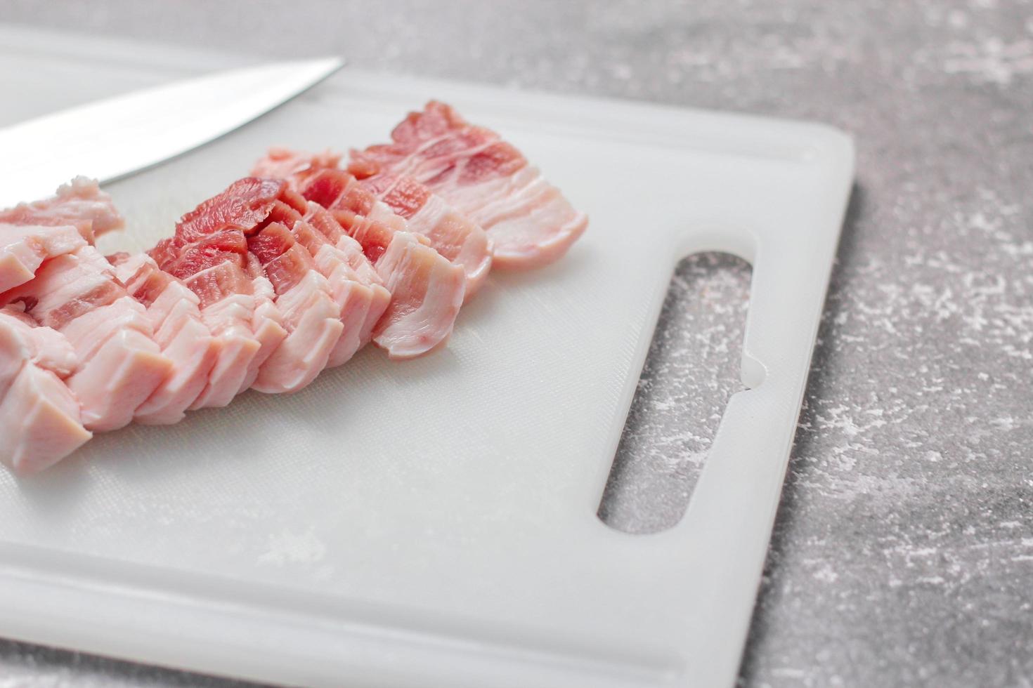 durchwachsenes schweinefleisch wird auf einem weißen schneidebrett in der küche geschnitten. nahaufnahme schnittfolie schweinebauch roh foto