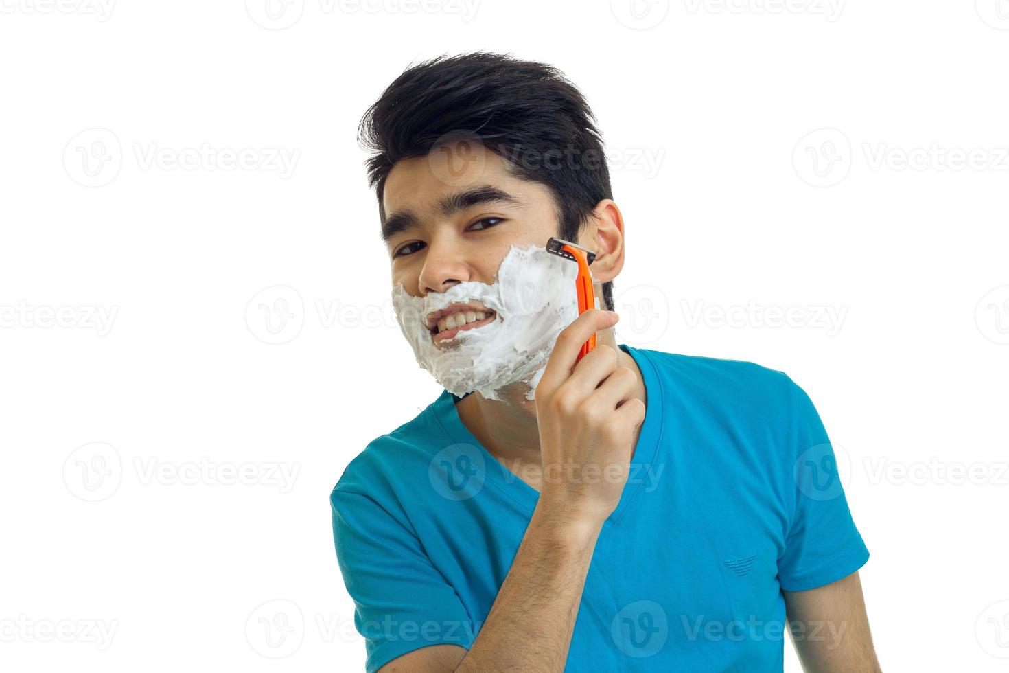 Fröhlicher wunderbarer Kerl mit Schaum auf seinem Gesicht rasiert Maschine und lächelt foto