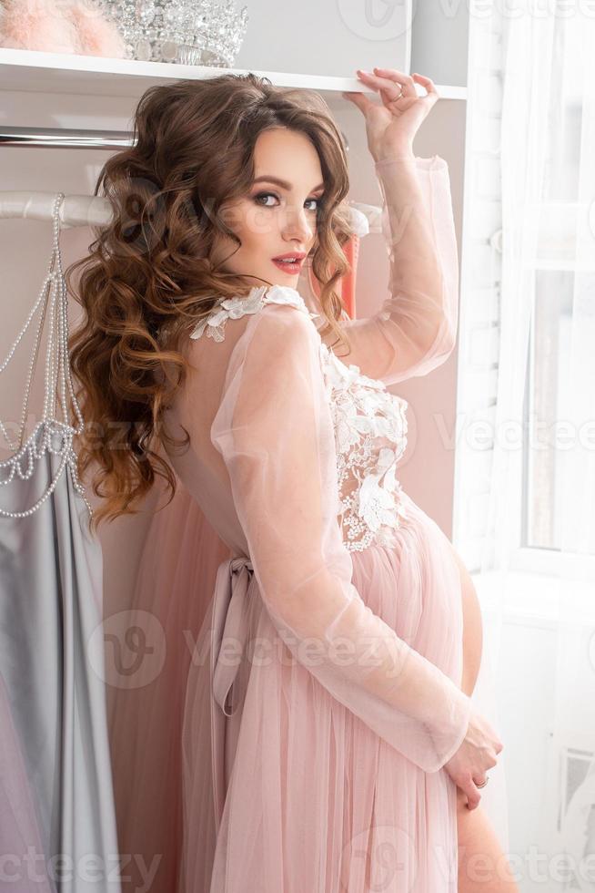 schöne schwangere dame in einem rosa kleid zu hause foto