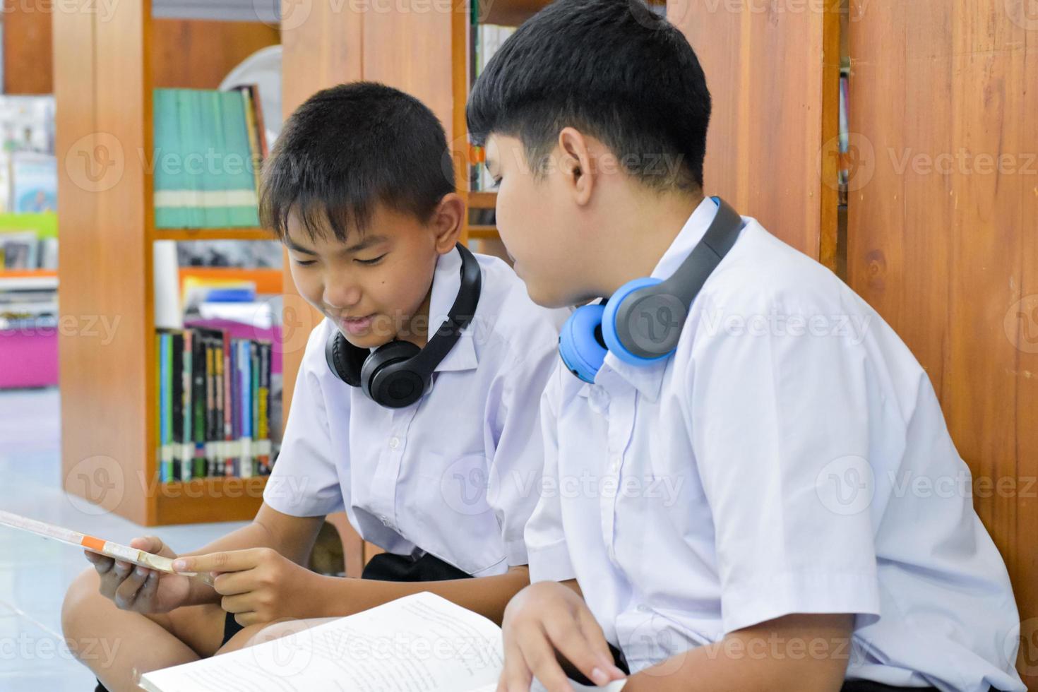 soft fucus von zwei asiatischen jungen studenten hören medien, lesen und beraten sich über lieblingsbücher in der schulbibliothek foto