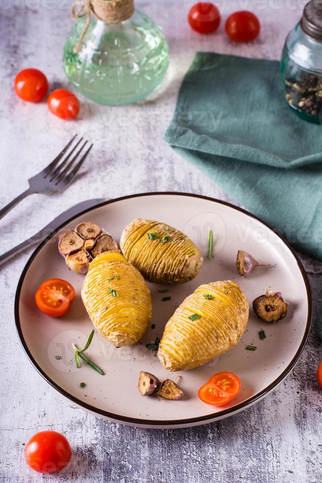 Gebackene Hasselback-Kartoffeln mit Knoblauch und Rosmarin auf einem Teller. hausgemachtes Mittagessen. vertikale Ansicht foto