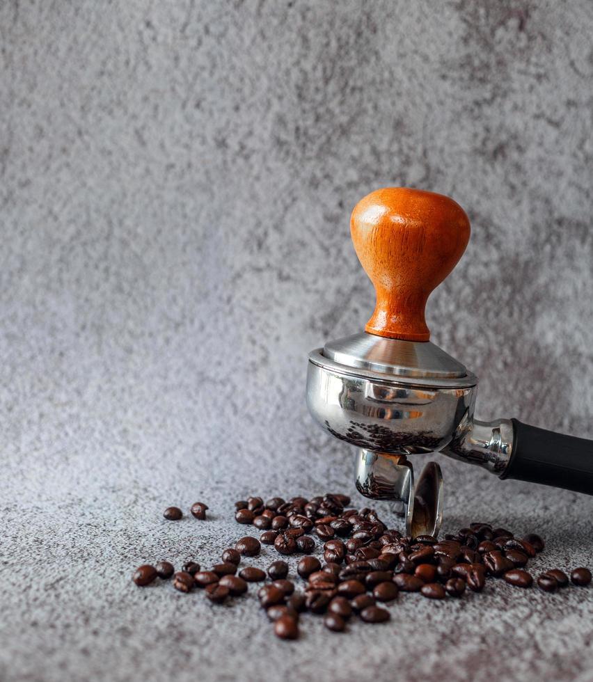 Ausrüstung in einem Café von Barista Coffee Tool Portafilter mit Tamper und dunkel gerösteten Kaffeebohnen auf grauem Hintergrund foto