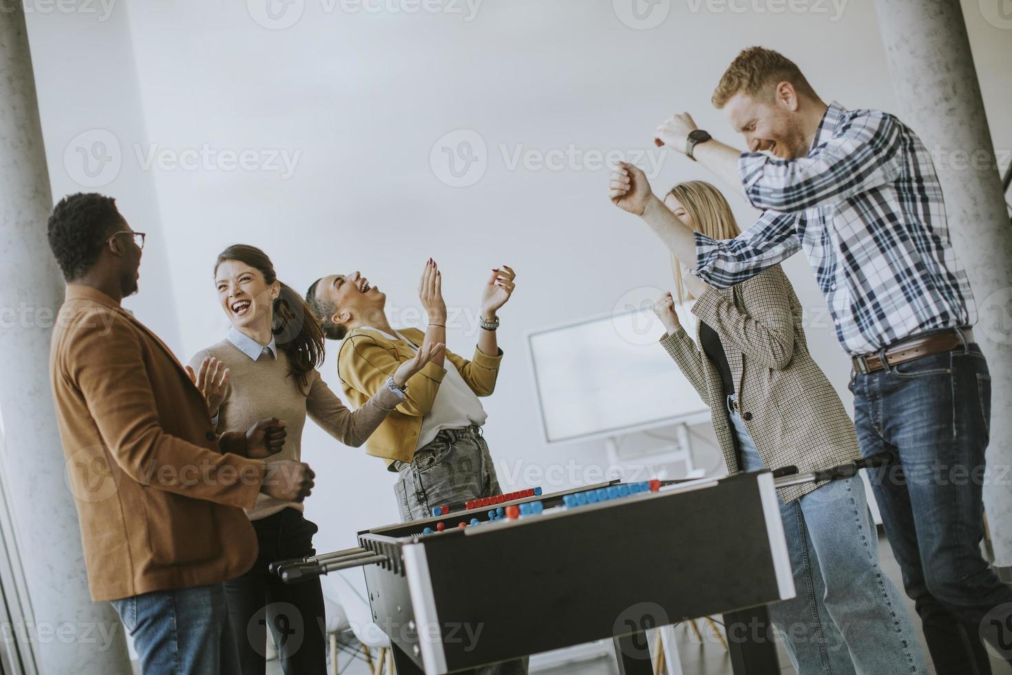 Junge lässige multiethnische Geschäftsleute, die Tischfußball spielen und sich im Büro entspannen foto