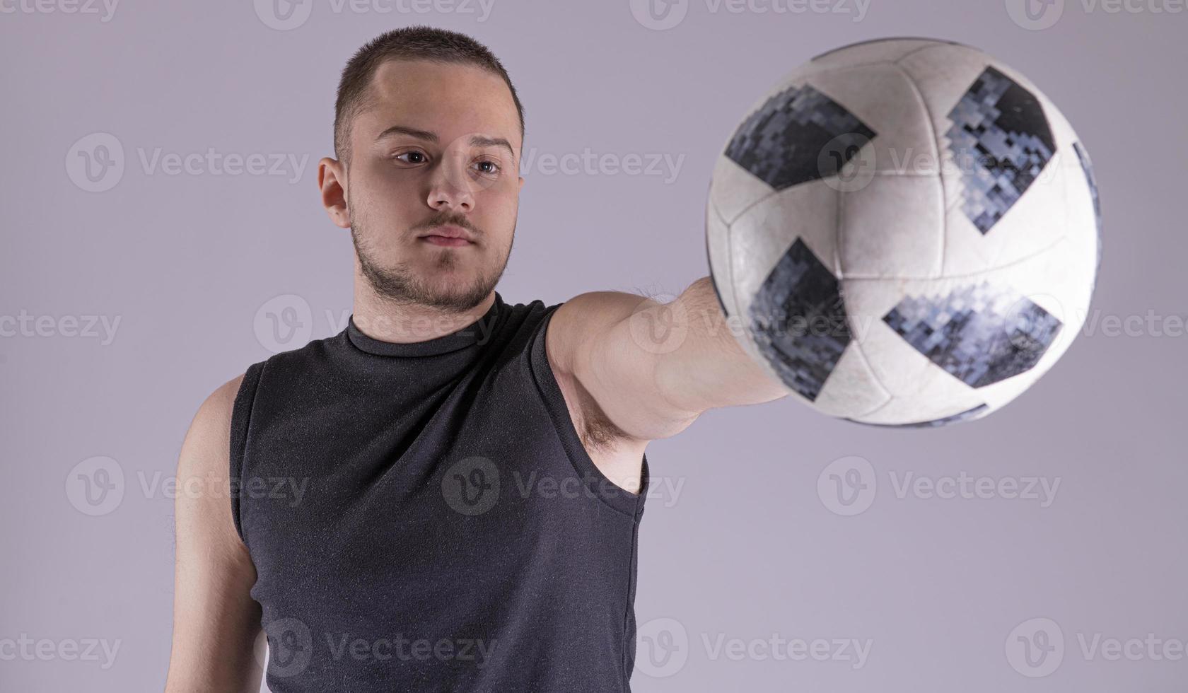 junger glücklicher mann 20er fan support fußball sportmannschaft halten in der hand fußball. getrennt auf normalem festem grauem Hintergrund foto