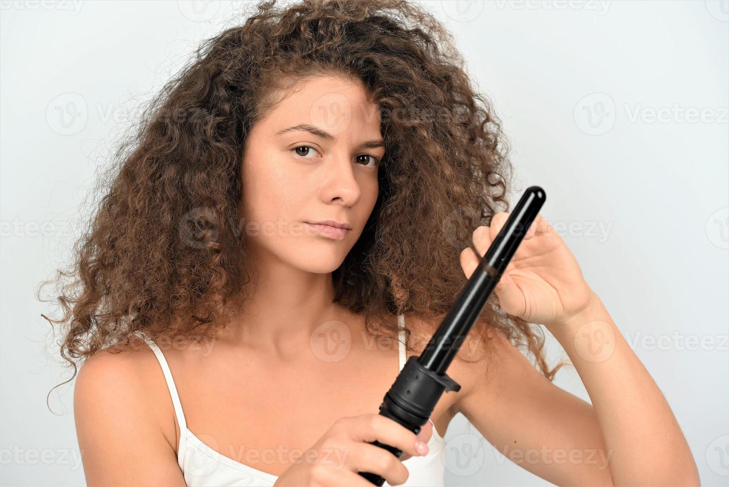 Schöne lächelnde Frau mit langem, gewelltem Haar, die es mit Lockenstab bügelt. glückliches Mädchen mit wunderschönem, gesundem, glattem Haar mit Lockenwickler für perfekte Locken. Frisur und Friseur foto