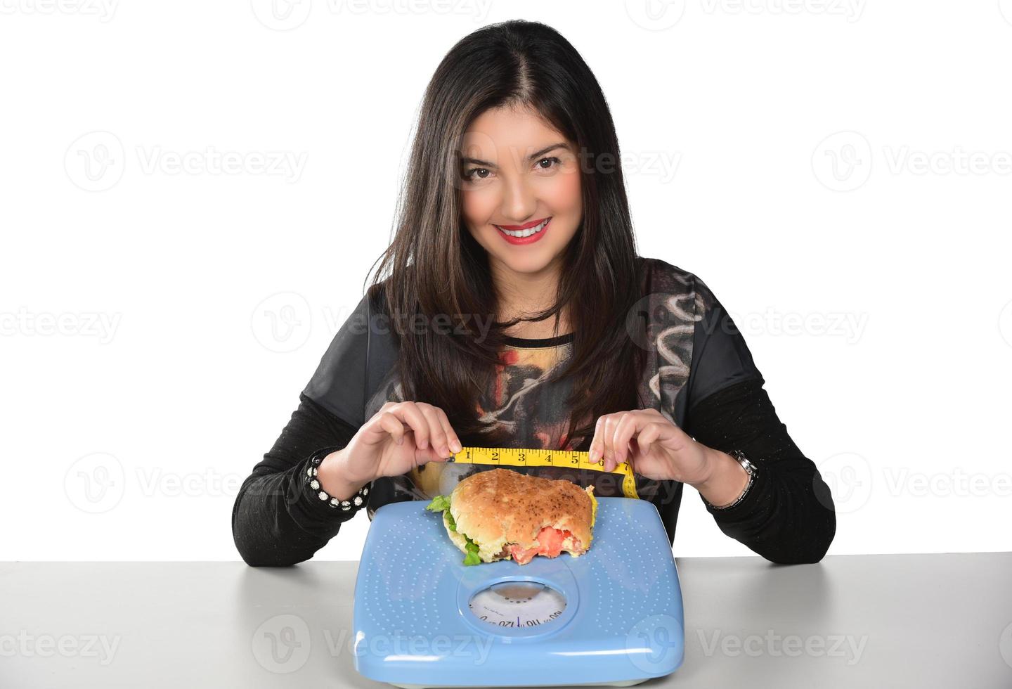 Porträt eines schönen lustigen jungen Mädchens auf dem weißen Hintergrund, das einen Tablettburger mit Hamburger und Messskala hält foto