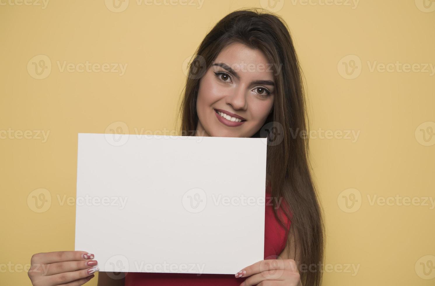 junge lächelnde frau, die ein leeres blatt papier für werbung hält foto