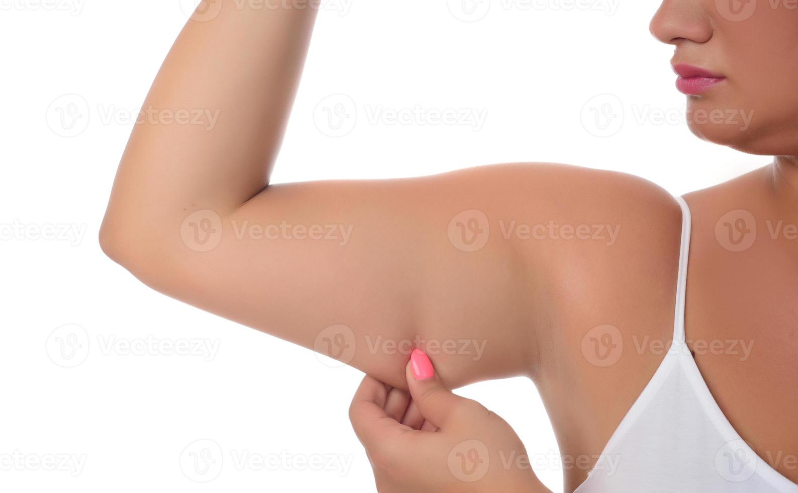 Frau, die ein Fett auf ihren Armen auf weißem Hintergrund einklemmt foto