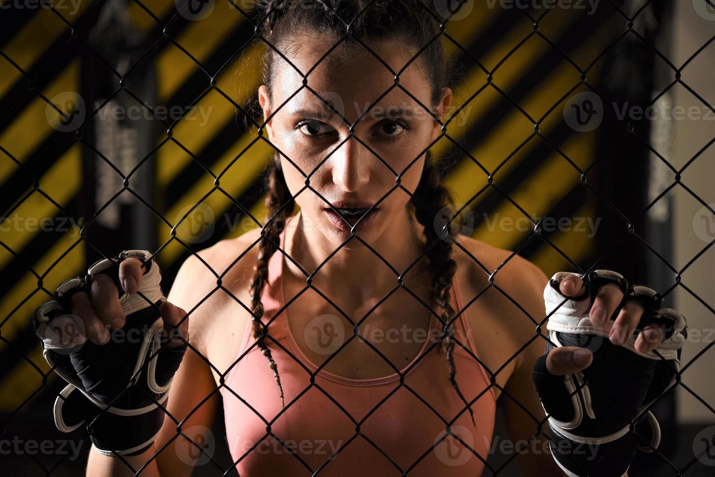Eine weibliche Auszubildende gemischter Kampfkünste, die eine Handpackung trägt, wärmt sich im Ringkäfig auf, indem sie ihren Rücken und ihre Beine streckt. foto
