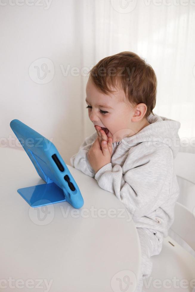 glücklicher kleiner junge, der zu hause ein spiel auf einem digitalen tablet spielt. Porträt eines Kindes zu Hause, das Zeichentrickfilme auf dem Tablet ansieht. moderne kinder- und bildungstechnologie. foto