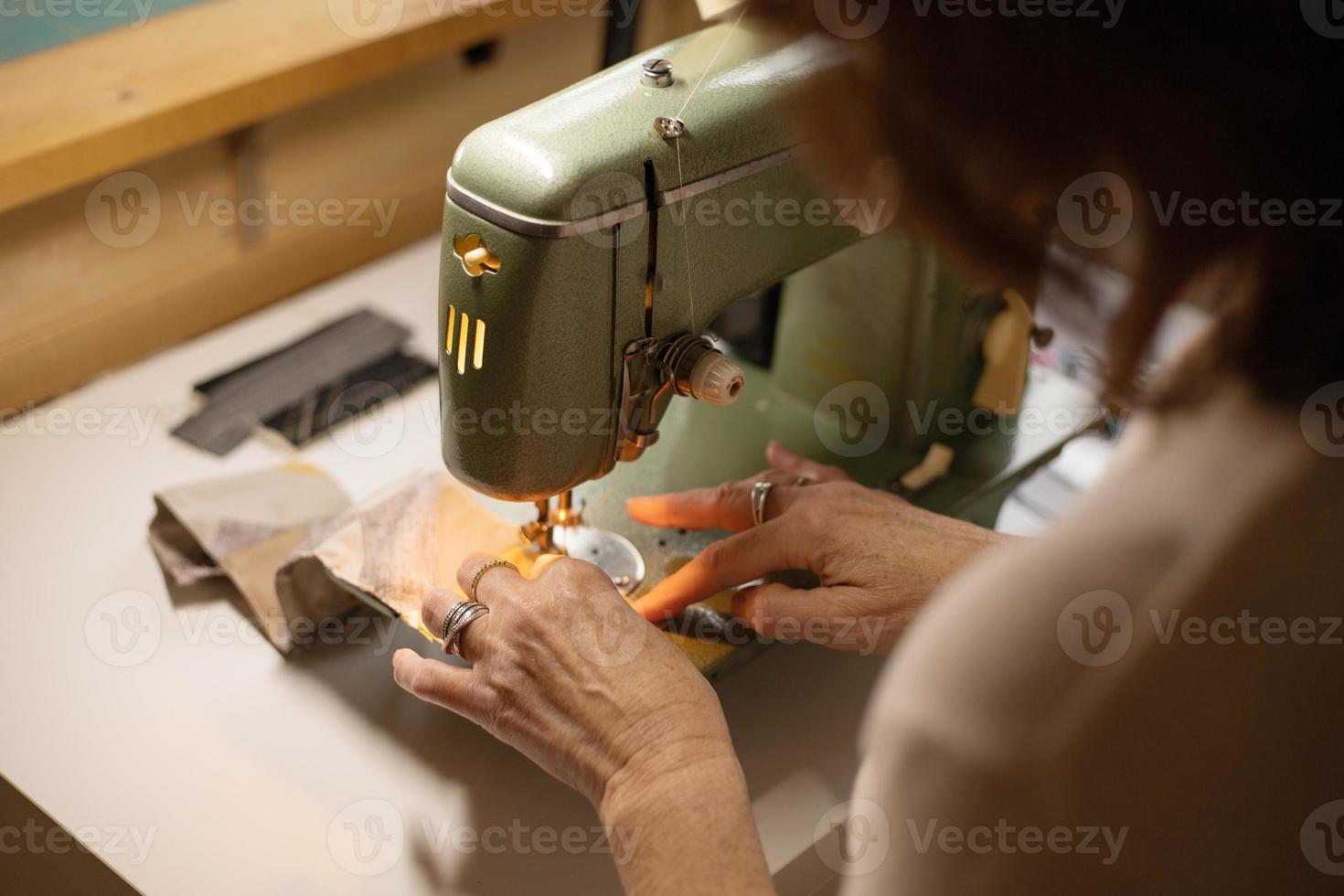 Nahaufnahme der Hände der Frau, die Stoff mit einer Vintage-Retro-Nähmaschine nähen. Mode, Kreation und Schneiderei. Nähprozess im Atelier oder in der Werkstatt. foto