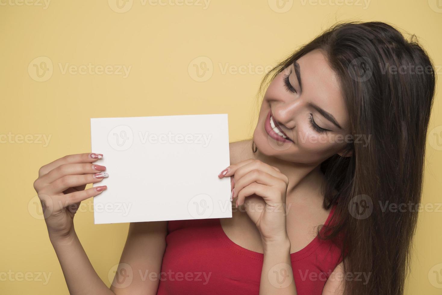 junge lächelnde frau, die ein leeres blatt papier für werbung hält foto