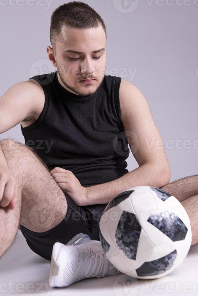 junger glücklicher mann 20er fan support fußball sportmannschaft halten in der hand fußball. getrennt auf normalem festem grauem Hintergrund foto