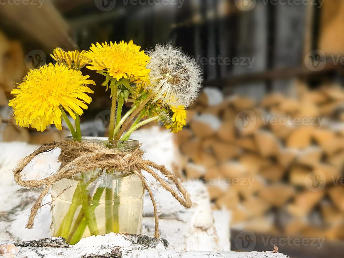 Holzstapel aus Birkenbrennholz. ein blumenstrauß aus gelben und weißen löwenzahn in einem glas. Vorbereitung von Holz für den Ofen. foto