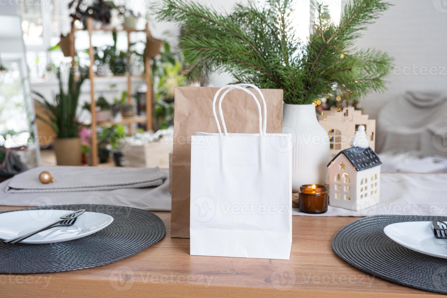 papierpakete mock-up sind auf dem küchentisch serviert, der für weihnachten dekoriert ist. Einkäufe und Geschenke, Geschenke und Fertiggerichte werden geliefert und für das neue Jahr zubereitet foto