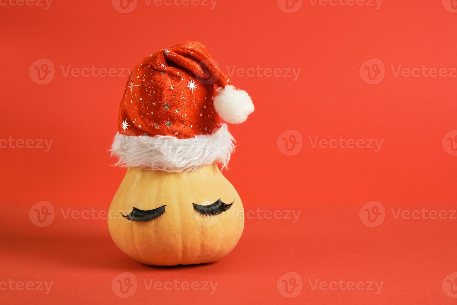 Kürbis in Weihnachtsmütze und falsche Wimpern auf rotem Hintergrund foto