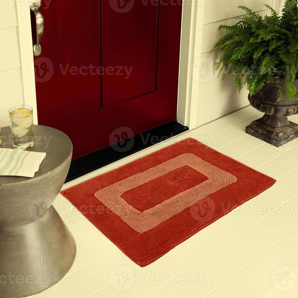 Designer-Willkommenseingangs-Fußmatte auf dem Boden vor der Eingangstür mit Pflanzen und Zitroneneisgetränk foto