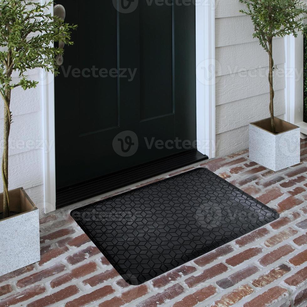 Designer-Willkommenseingangs-Fußmatte auf massivem Ziegelboden vor der Eingangstür mit Pflanzen foto
