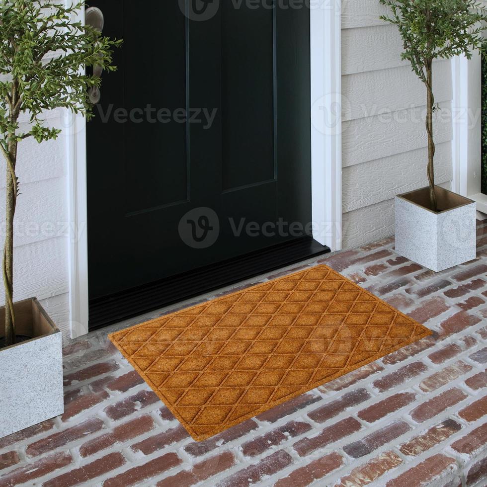 Designer-Willkommenseingangs-Fußmatte auf massivem Ziegelboden vor der Eingangstür mit Pflanzen foto