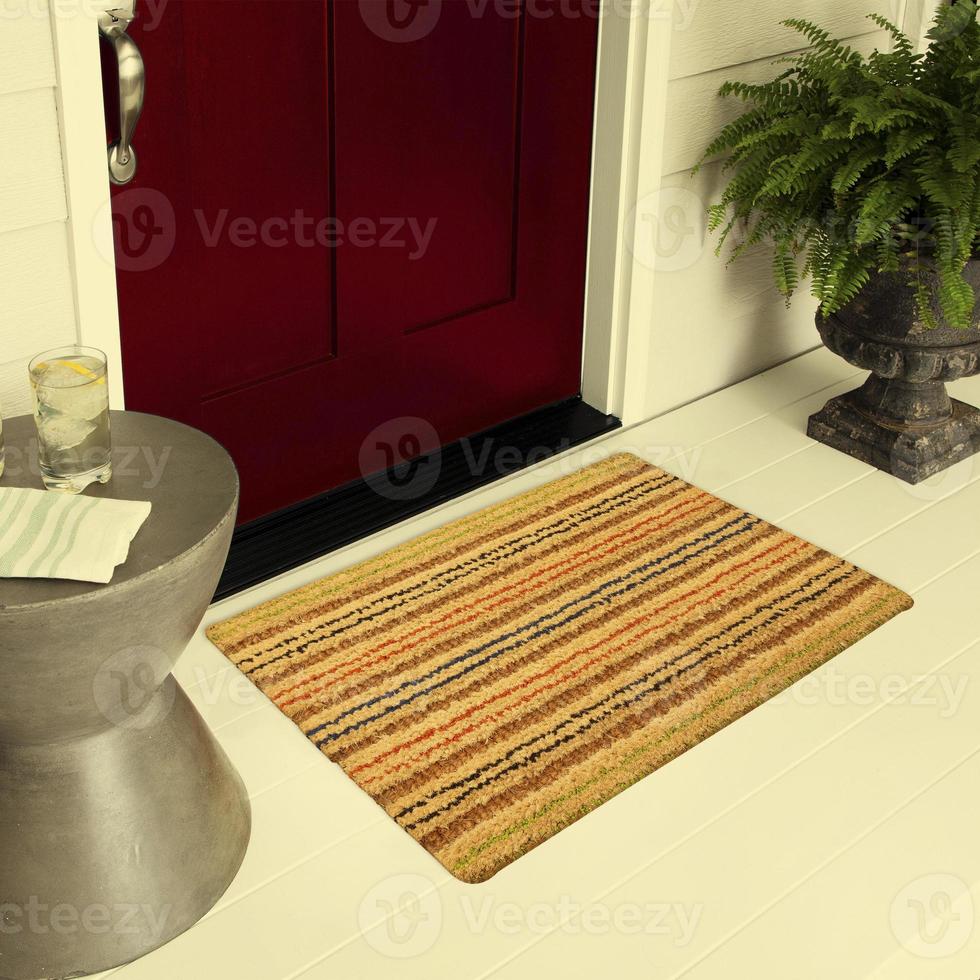 Designer-Willkommenseingangs-Fußmatte auf dem Boden vor der Eingangstür mit Pflanzen und Zitroneneisgetränk foto