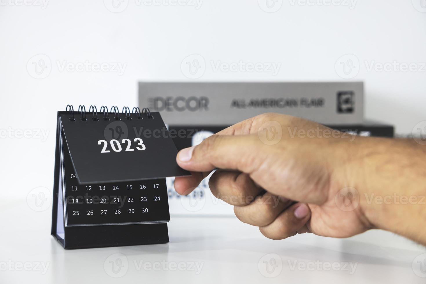 hand, die den geschäftskalender 2023 auf dem bürotisch am neujahrstag hält. Erstellen Sie einen Arbeitsplan für den Jahresanfang. konzept über feier, geschäft, weihnachten, neujahr. foto