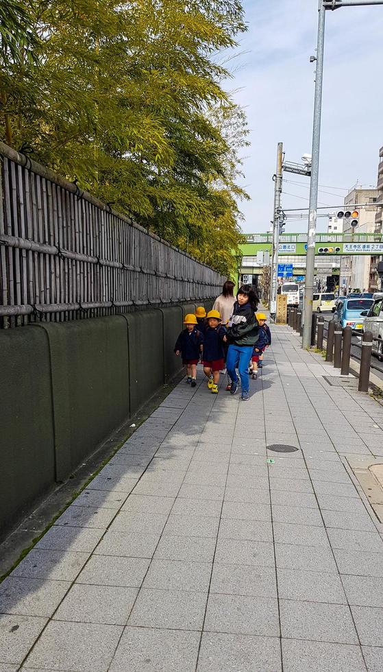 osaka, japan am 9. april 2019. einige japanische kindergartenkinder gehen auf einem bürgersteig auf einer straße in osaka foto