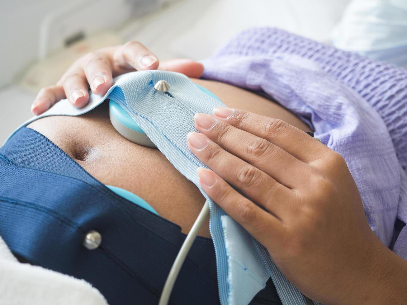 Nahaufnahme einer schwangeren Frau auf dem Bett, die das Baby mit medizinischen Geräten im Krankenhaus überprüft foto