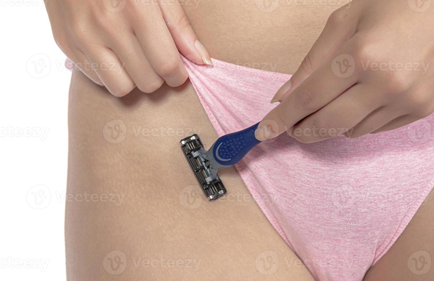 ein mädchen in rosa höschen rasiert sich mit einem rasierer die haare im bikinibereich und macht eine enthaarung mit creme foto