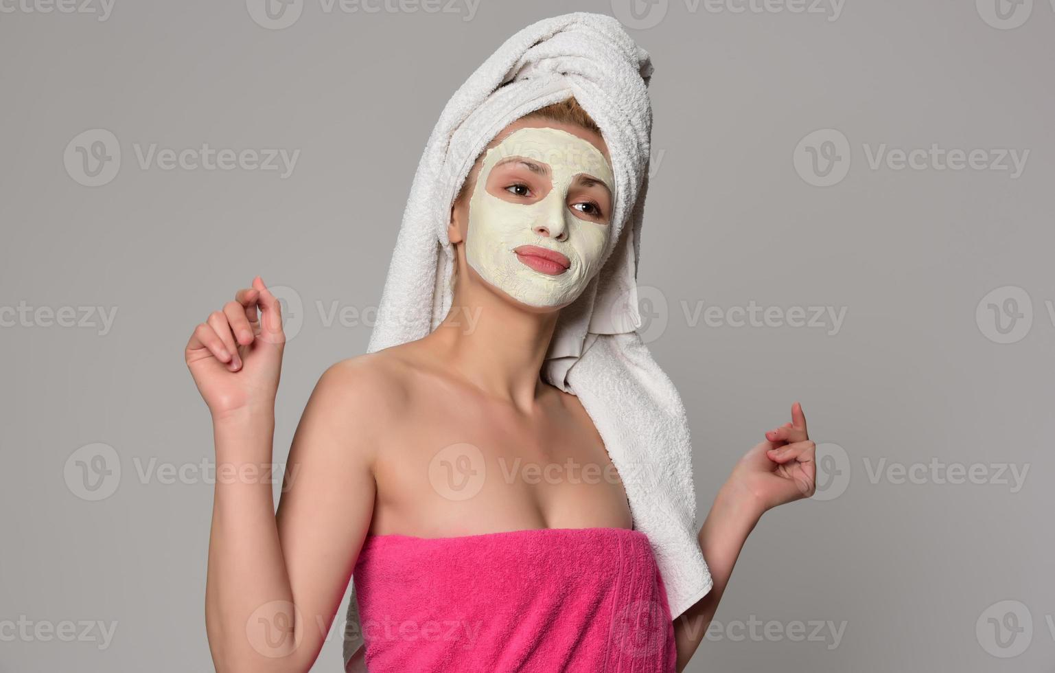 Schönes weibliches Modell mit Handtuch auf ihrem Ohr und weißer kosmetischer Gesichtsmaske auf ihrem Gesicht. Beauty-Kosmetik-Konzept. isoliert auf grauem Hintergrund. foto