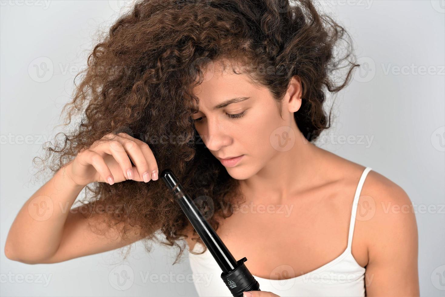 Schöne lächelnde Frau mit langem, gewelltem Haar, die es mit Lockenstab bügelt. glückliches Mädchen mit wunderschönem, gesundem, glattem Haar mit Lockenwickler für perfekte Locken. Frisur und Friseur foto