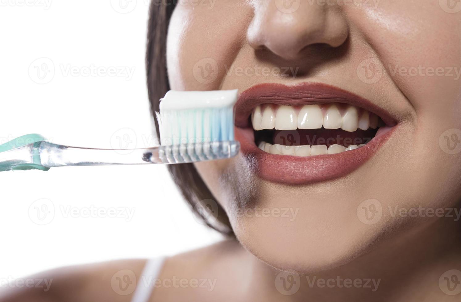 Porträt einer attraktiven lächelnden Frau, die auf einer weißen Studioaufnahme isoliert ist, die ihre Zähne putzt foto