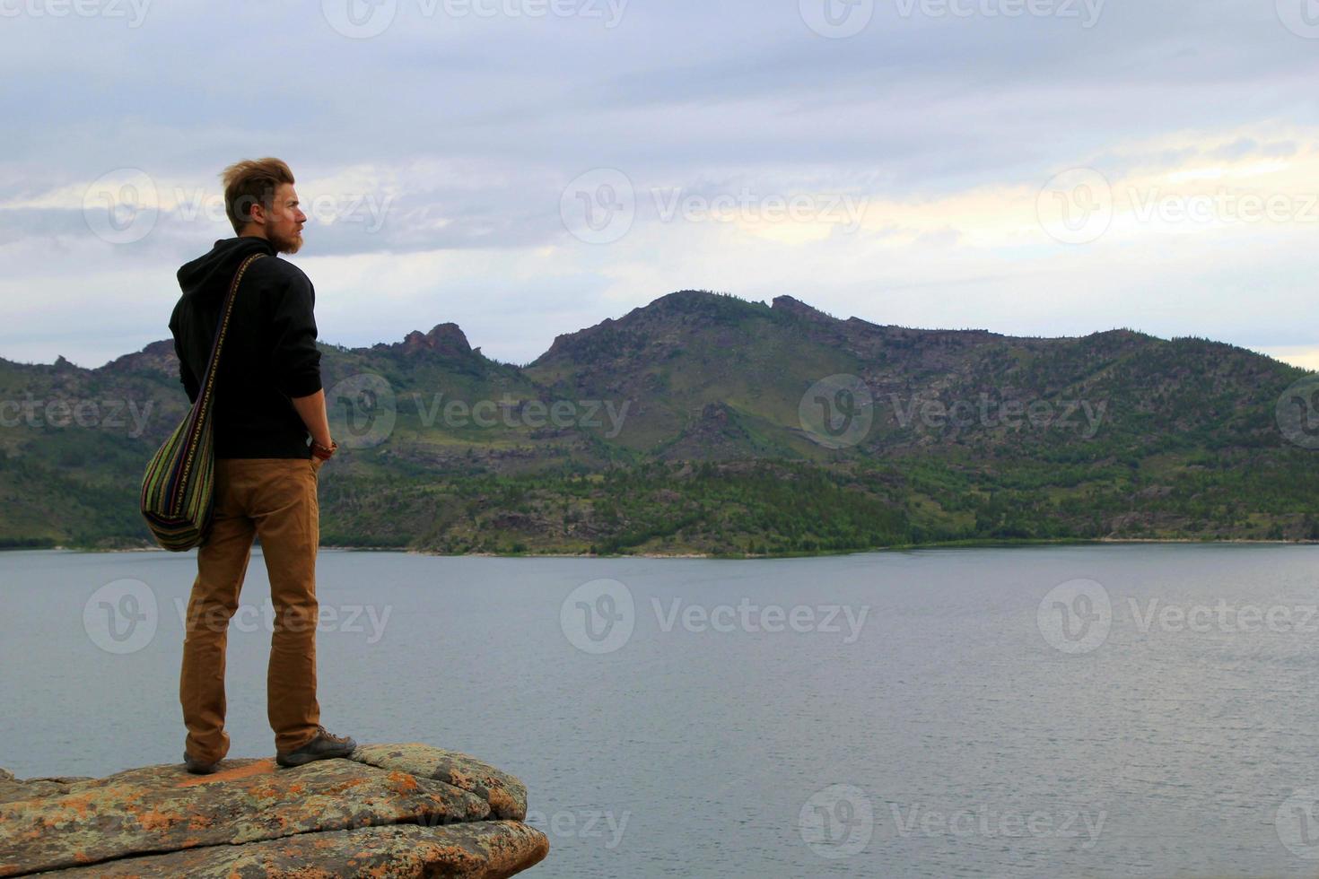 reise nach kasachstan, bayanaul nationalpark. der junge mann schaut in die ferne auf einen see und berge. foto