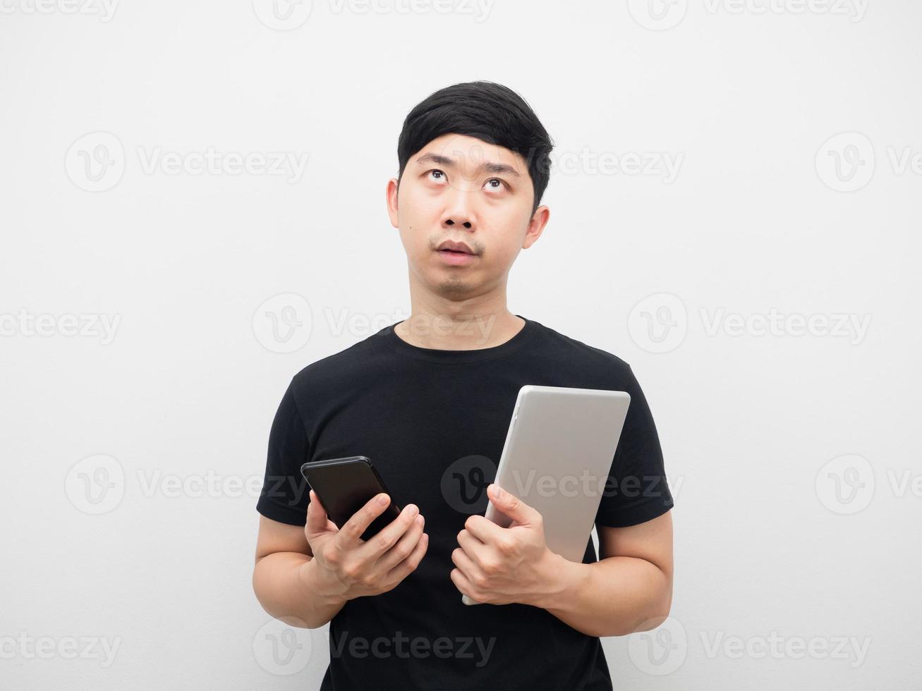 asiatischer mann, der tablette mit handy hält, fühlt sich gelangweilt, oben zu schauen foto