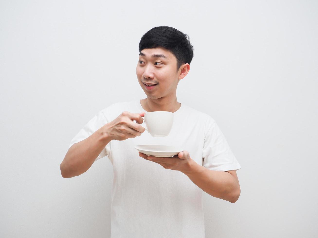 asiatischer mann hält kaffeetasse in der hand und schaut mit glücklichem lächeln auf weißem hintergrund auf die linke seite foto