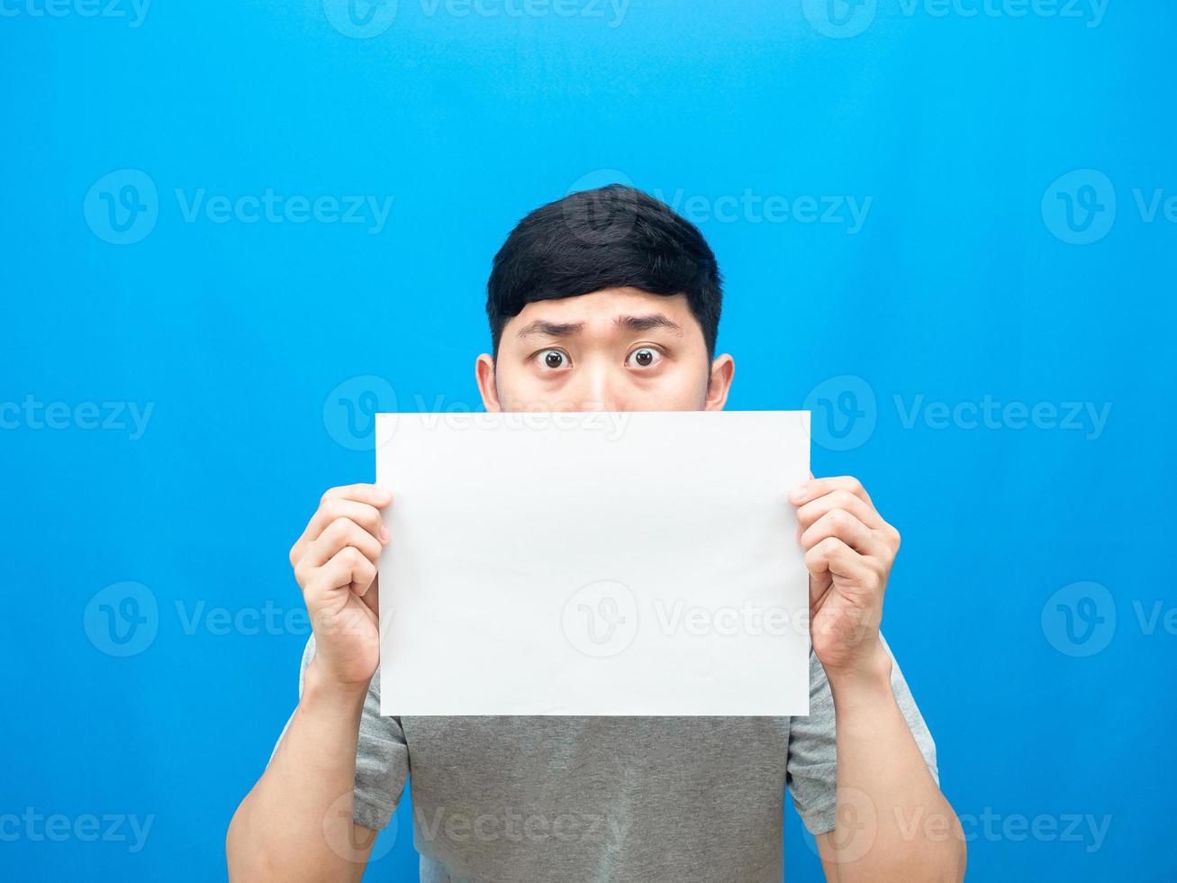 mann, der leeres blatt hält, schließt sein gesicht auf blauem hintergrund foto