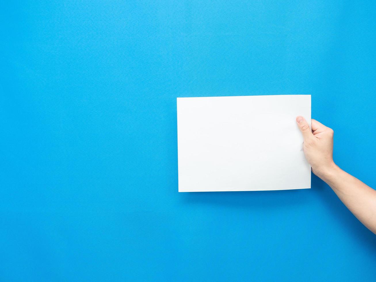 Mannhand, die leeres Blatt auf blauem Hintergrund hält foto