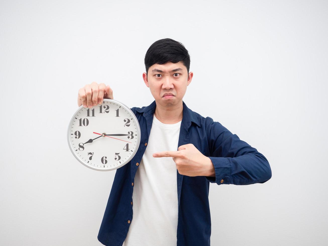 asiatischer Mann wütendes Gesicht zeigt um 15 Minuten nach 8 Uhr auf die Uhr. in seiner Hand arbeitet spät Konzept auf weißem Hintergrund foto