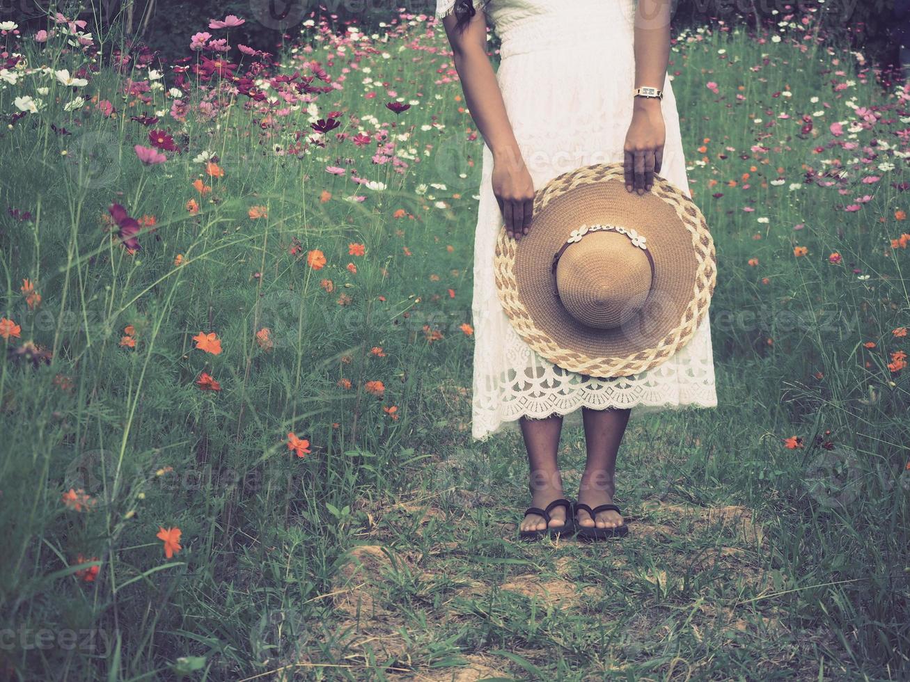 reisende frau, die im blumenpark steht und hut mit schöner aussicht hält, asiatin reisendes weißes kleid im blumengarten foto