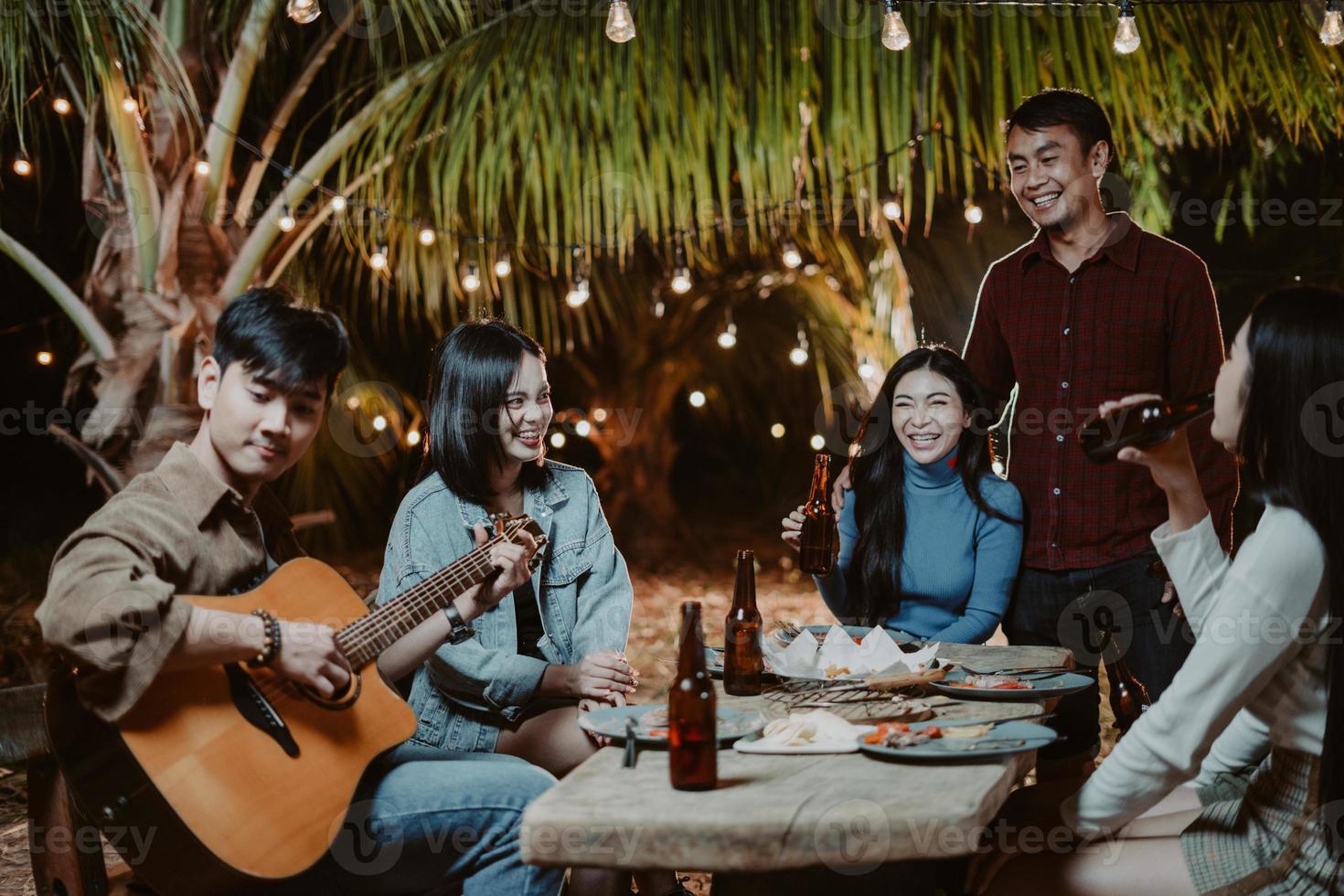 asiatische gruppenleute, die auf der party gitarre spielen und bier trinken foto