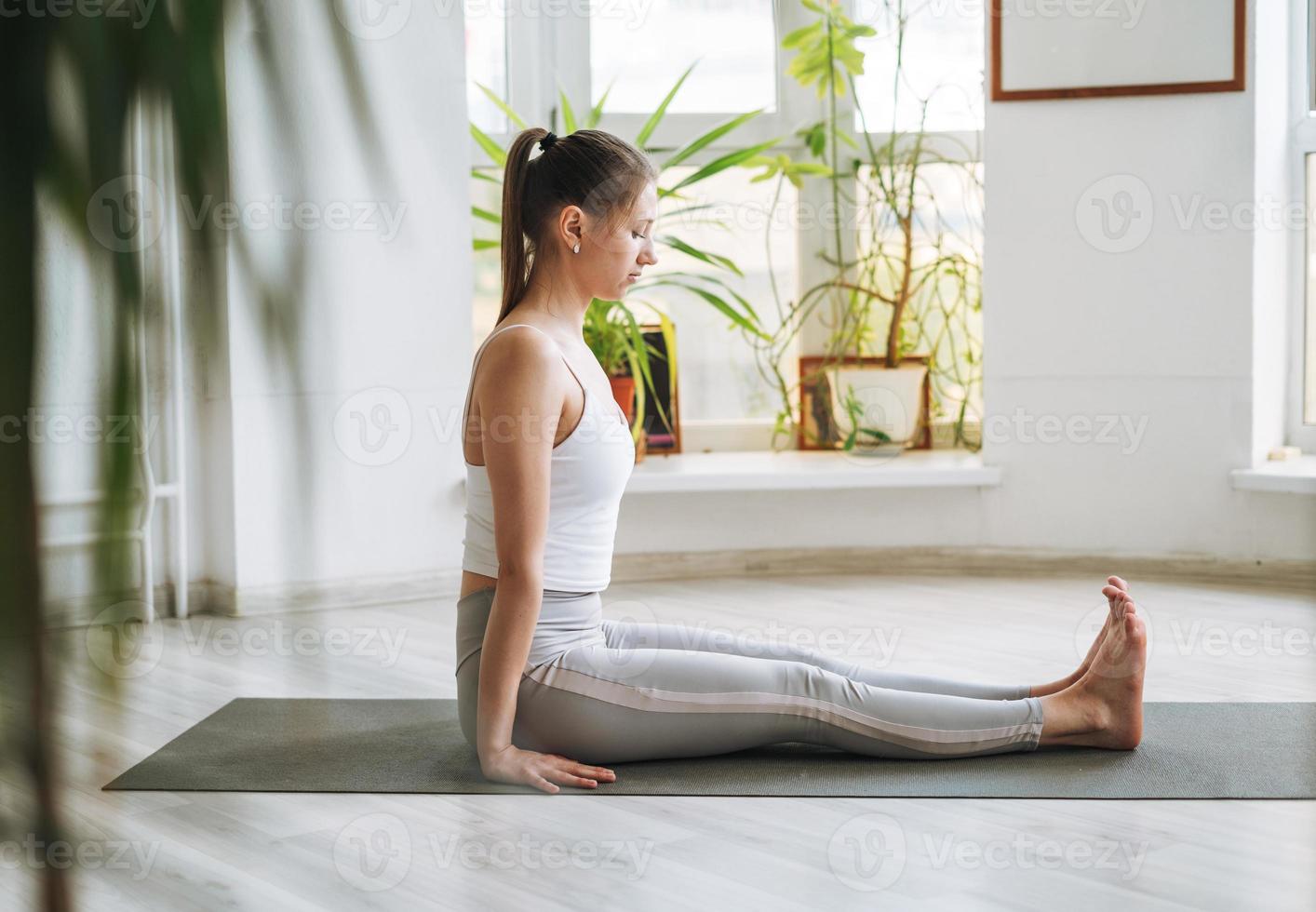 Junge fitte Frau praktiziert Yoga und macht Asanas in einem hellen Yogastudio mit grünen Zimmerpflanzen foto