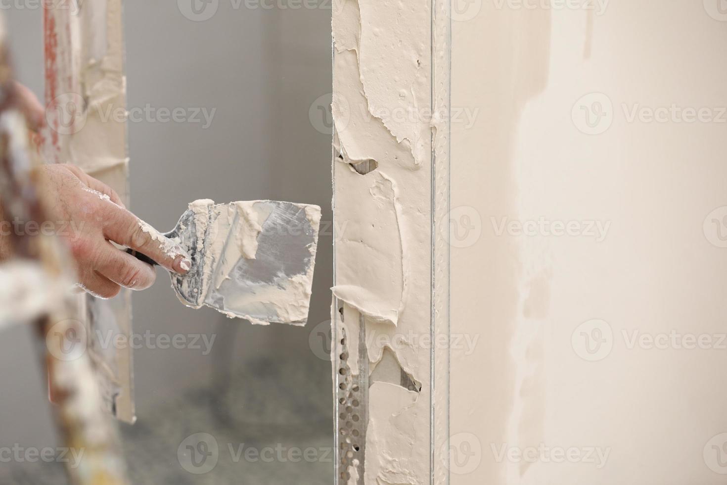 Baumeister mit einer Kelle, um Putz hinzuzufügen. Verputzwand mit Spachtel, Nahaufnahme. Befestigung der Wandoberfläche und Vorbereitung zum Streichen. Bauarbeiten während der Quarantäne foto