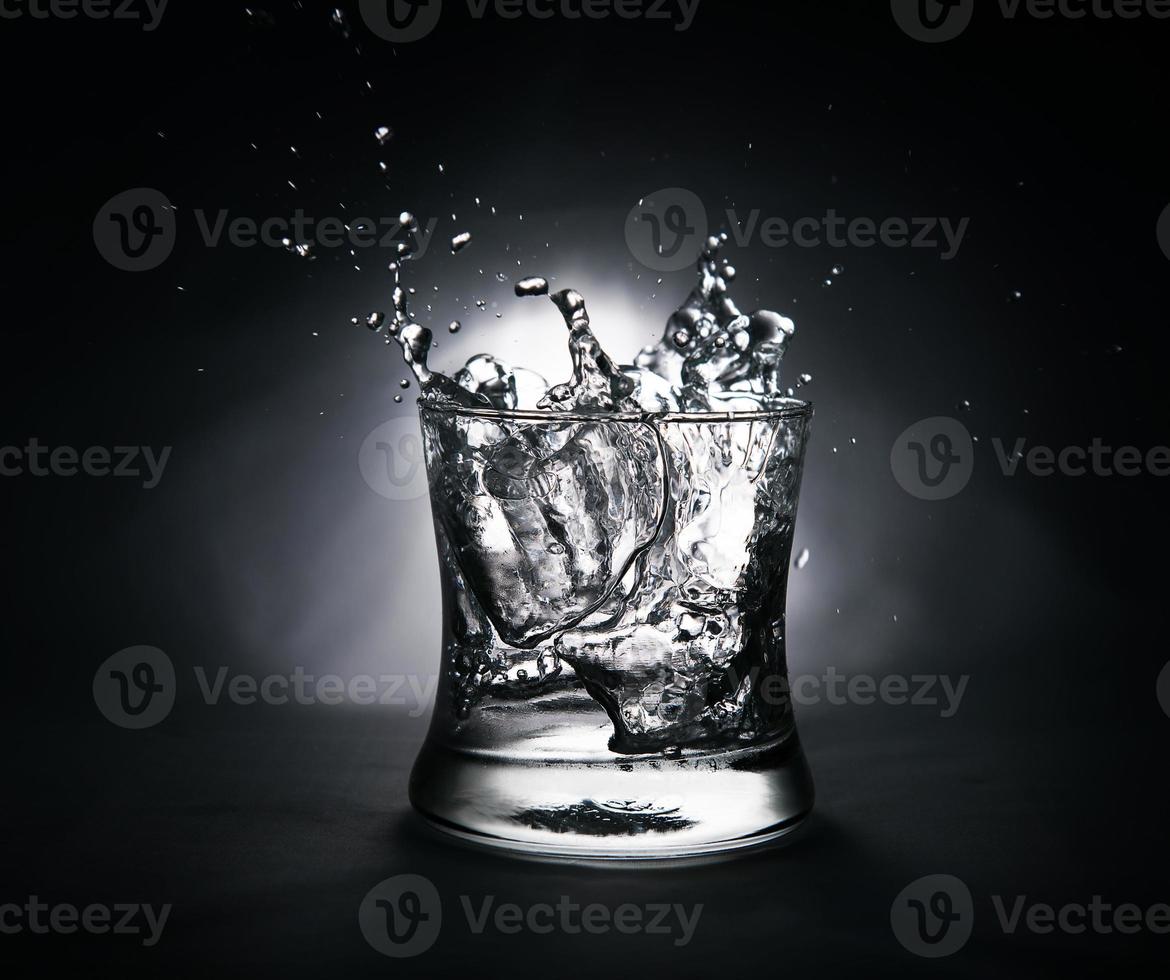 Eiswürfel, der in ein mit Wasser gefülltes Glas spritzt foto