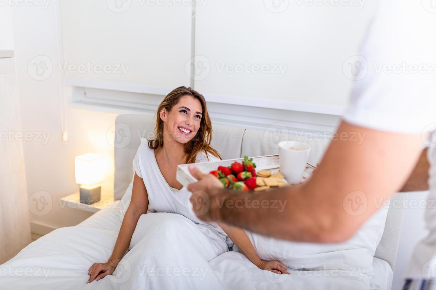 guten morgen gesundes frühstück im bett. Schöne junge Frau liegt im Bett, während ihr gutaussehender Mann leckeres Frühstück bringt. foto