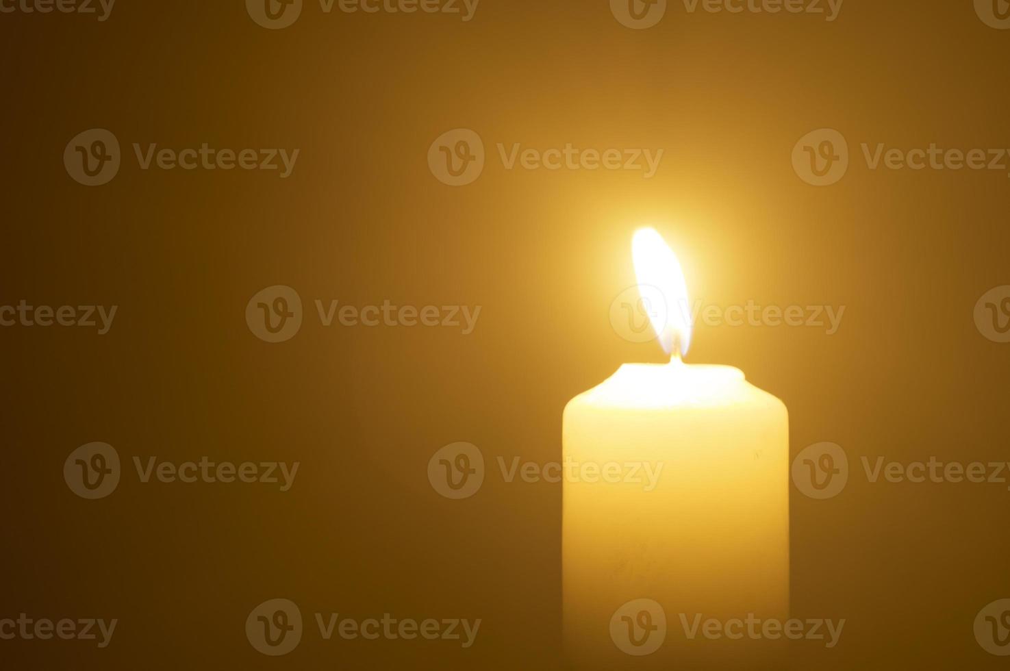Verschwommenes Foto einer einzelnen brennenden Kerzenflamme oder eines Lichts, das auf einer gelben Kerze auf orangefarbenem oder rotem Hintergrund auf dem Tisch in der Kirche zu Weihnachten, Beerdigung oder Gedenkfeier leuchtet