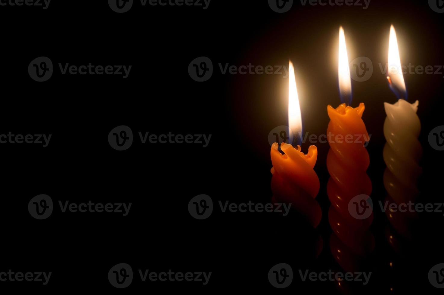 drei brennende kerzenflammen oder lichter, die auf spiralförmigen weißen und orangefarbenen kerzen auf schwarzem oder dunklem hintergrund auf dem tisch in der kirche zu weihnachten, beerdigung oder gedenkfeier leuchten foto