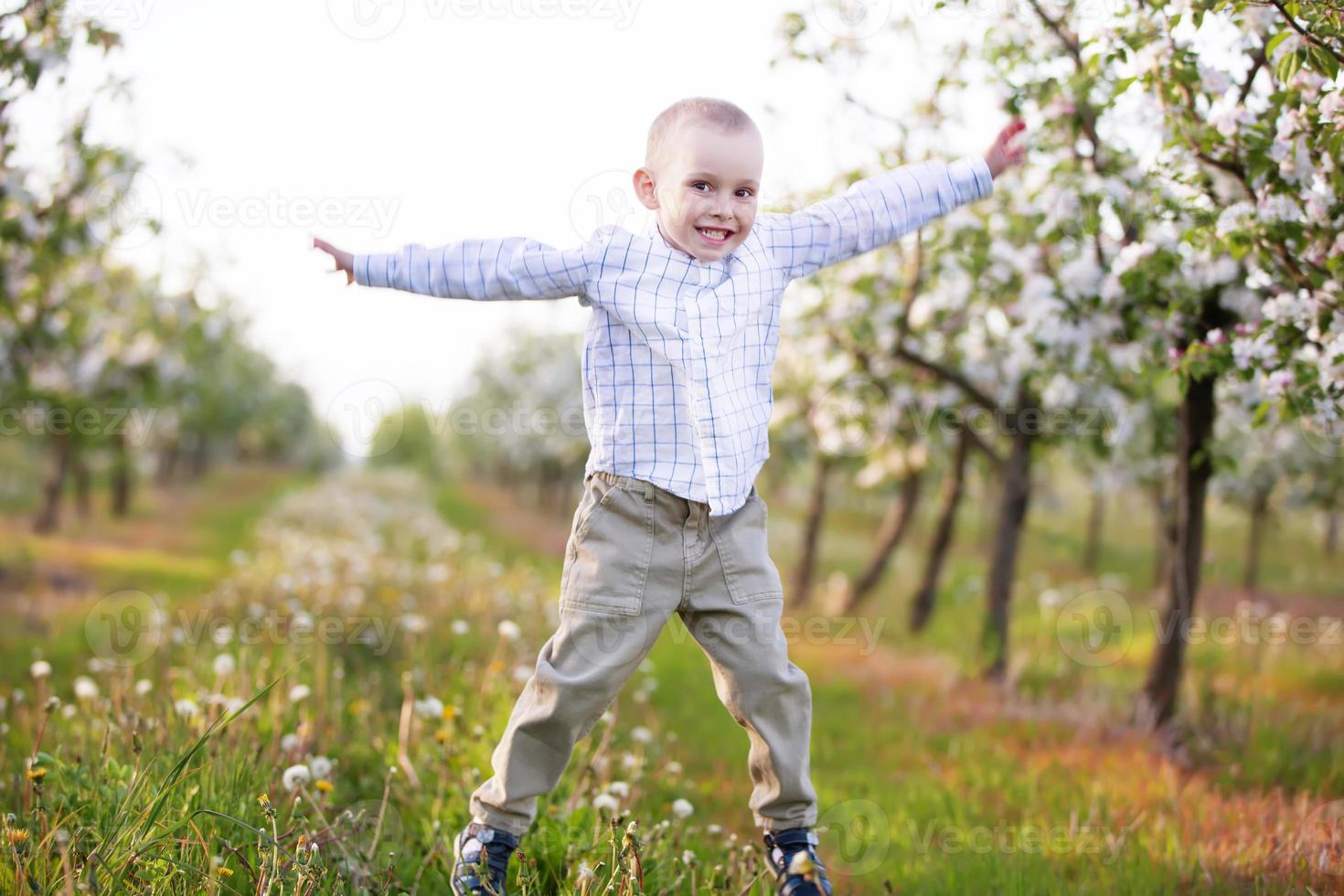 ein fröhliches kind in einem blühenden frühlingsgarten spielt, springt, er hat gute laune. foto