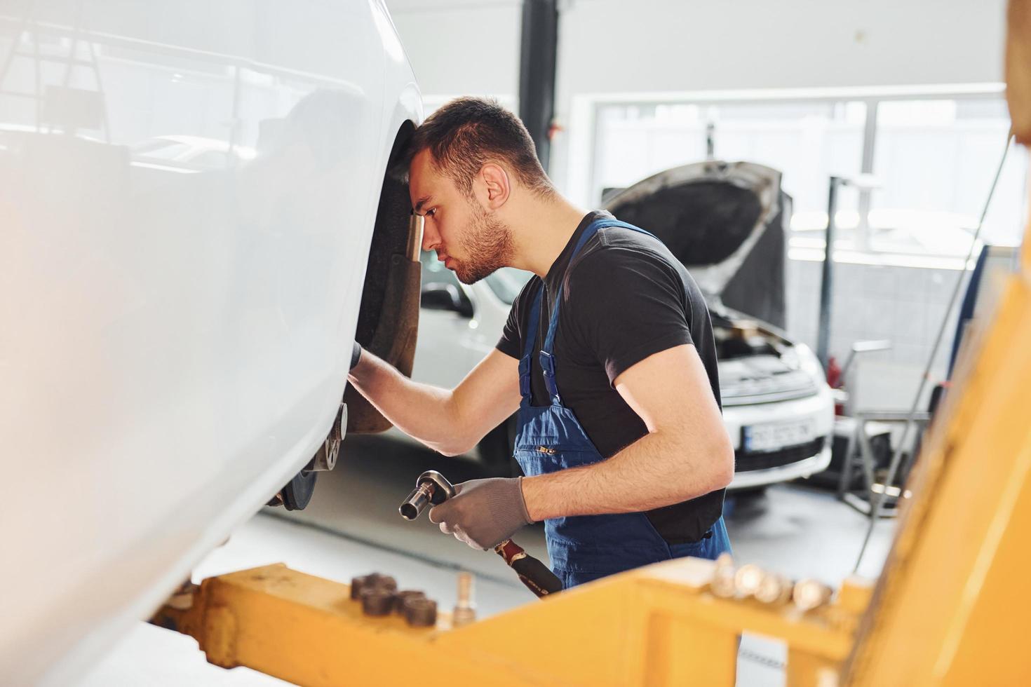 Mann in Arbeitsuniform repariert Auto drinnen. Konzept des Autoservices foto