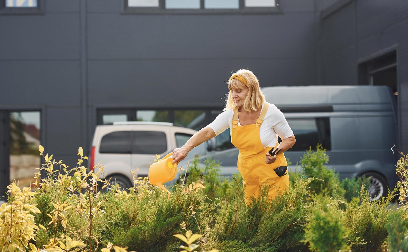 Seniorin in gelber Uniform ist tagsüber im Garten und gießt Pflanzen foto