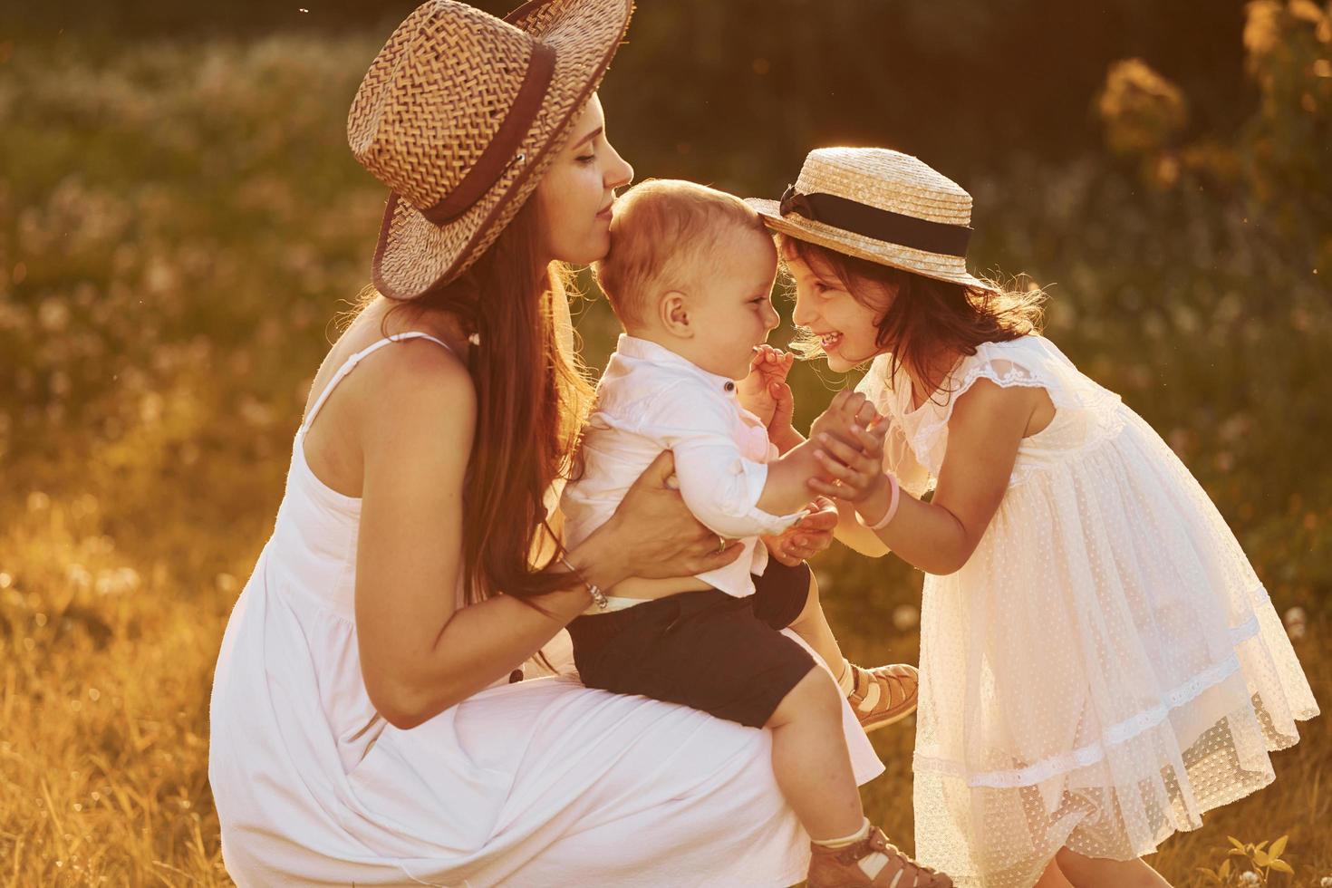 glückliche familie von mutter, kleinem sohn und tochter, die an sonnigen sommertagen freizeit auf dem feld verbringen foto